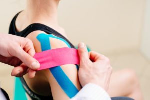 Woman's shoulder being taped by a physician due to shoulder impingement