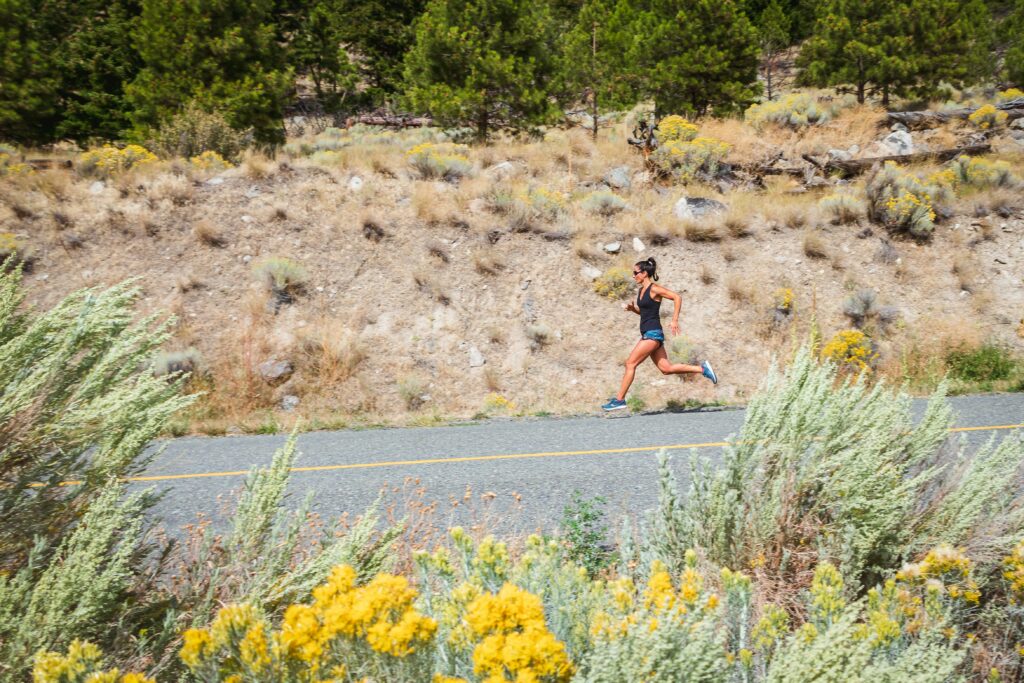 Woman running on the road in the high desert country. Sagebrush and yellow flowers at the forefront.